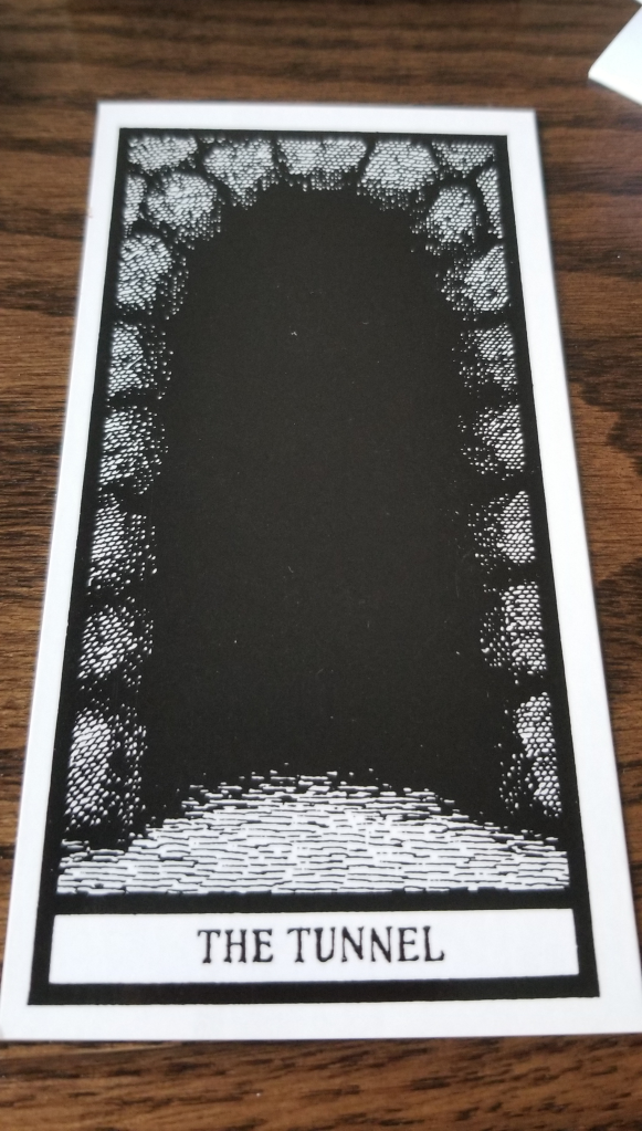 Grayscale tarot card depicting a stone arch entry to a pitch black tunnel. The Tunnel printed at the bottom in a gothic font.
